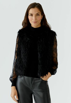 Black faux fur vest with a high collar over a black lace long-sleeve top, paired with black leather pants. Smooth and textured materials.