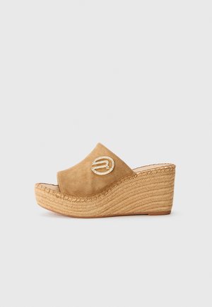 Sandalias de cuña de ante color beige con base de yute trenzado, con un detalle dorado decorativo en la parte superior. Diseño con punta abierta.