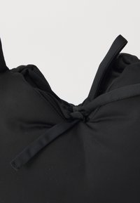 Črna platnena torba z teksturirano, rebrasto površino in dvema povezanima trakoma. Torba ima mehak, zaobljen oblik in zbrano zgornjo stran.