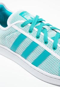 Närbild av en vit och turkos Adidas-sko med meshtyg, randiga detaljer och turkosa snören knutna i en rosett.