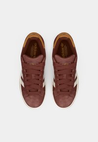 Mørkerøde ruskindsneakers med hvide striber, rund tå og brune accenter. Har flade snørebånd og en tekstureret sål. Adidas-logo på tungen.