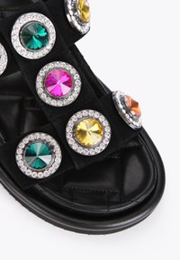 Sandalo nero con numerosi grandi gioielli rotondi in verde, rosa, giallo, arancione e trasparente, incastonati in anelli color argento su una tomaia morbida.