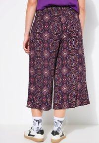 Gemusterte Culottes mit lila Grundfarbe und aufwendigen Blumendesigns in Rot, Blau und Weiß, kombiniert mit weißen Socken und Turnschuhen.