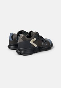 Sneaker neri e grigi eleganti con suola arrotondata, dettagli in pelle testurizzata e rete, caratterizzati da blocchi di colore unici e sovrapposizioni decorate.