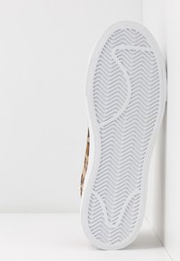 Semelle unique de basket vue de face avec bande de roulement en caoutchouc blanc et motif en chevrons, côtés de la chaussure à imprimé léopard partiellement visibles.