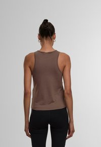 Brun ärmlös linne med figurnära passform, rundad halsringning och mjukt tyg. Bärs med svarta leggings, vilket ger en enkel design.