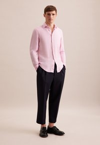 Camicia in lino rosa chiaro con colletto a punta, davanti con bottoni, abbinata a pantaloni tapered blu navy e scarpe nere stringate. Texture liscia.