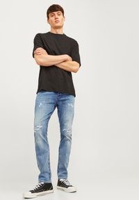 Camiseta negra de cuello redondo combinada con jeans desgastados de un azul claro y zapatillas altas negras con suelas blancas. Diseño de atuendo simple y casual.