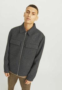 Veste à carreaux foncés en tissu texturé, dotée d'une fermeture éclair, de deux poches avant et d'un col. La coupe est décontractée.