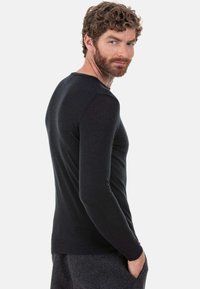 Schwarzes langärmeliges Strickoberteil mit schmaler Passform. Es verfügt über einen abgerundeten Ausschnitt und gerippte Bündchen und besteht aus weichem, atmungsaktivem Stoff mit glatter Textur.