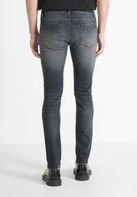 Mršavi traperice u tamnom izdanju s izblijedjelim efektom. Imaju dva stražnja džepa i kontrastnu šavovi. Uparene s crnim obućom.