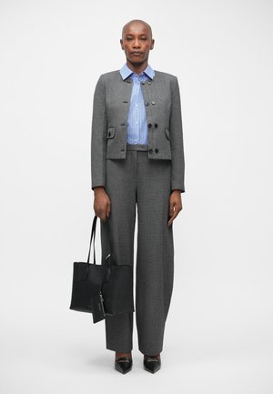 Blazer gris ajusté avec de grands boutons, chemise rayée bleue, pantalon gris à jambe large et sac fourre-tout noir. Des chaussures noires à bout pointu complètent la tenue.