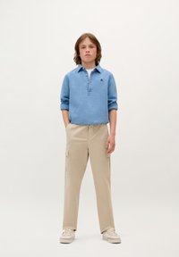 Lichtblauwe polo met lange mouwen en een drukknoopsluiting, gecombineerd met beige cargobroek met zijzakken en een relaxed fit.