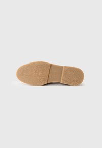 Semelle de chaussure en caoutchouc texturé beige, présentant une forme arrondie et une section centrale lisse. Aucune marque ou motif visible.