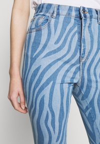 Jeans de mezclilla de color azul claro con un patrón de rayas de cebra en azul más oscuro. Tienen una cintura alta, bolsillos delanteros y detalles de costura en contraste.