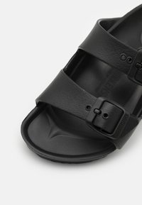 Schwarze Sandalen mit zwei verstellbaren Riemen und Metall-Schnallen. Hergestellt aus strukturiertem Material, mit einem konturierten Fußbett und einer flexiblen Sohle.