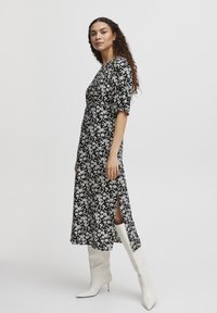 Robe midi noire à fleurs blanches, avec des manches courtes bouffantes, des fentes sur les côtés, associée à des bottes blanches jusqu'aux genoux. Texture de tissu lisse.