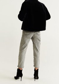 Veste en fausse fourrure noire, jean en denim gris avec revers de manches retroussées, et bottines noires à talons aiguilles. Le denim comporte des poches arrière et des coutures apparentes.