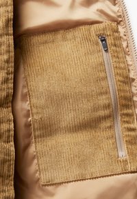 Ribbede mørkebrun corduroylomme med lodrette ribber, udstyret med en lynlåslukning på en glat, beige foring.