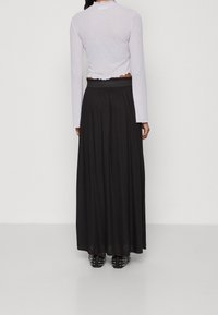 Lichtpaarse cropped top met lange mouwen en geplooide halslijn, gecombineerd met een zwarte, vloeiende maxi-rok en zwarte schoenen met studs.