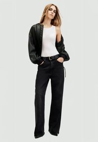 Black leather bomber jacket over a white tank top, paired with dark wide-leg jeans, featuring a belted waist and front pockets.