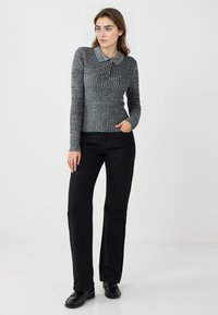 Grauer, gerippter Langarmoberteil mit Kragen, kombiniert mit schwarzen, geraden Hosen und schwarzen Slippern, die einen stimmigen, lässigen Look kreieren.