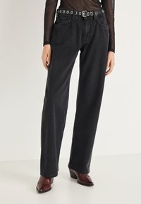 Čierne rifle s vysokým pásom, rovný strih, päť vreciek a opasok s cvočkami. Textúrovaná látka s hladkým povrchom.