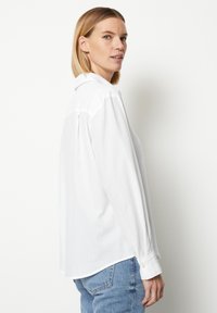 Weißes Langarmhemd mit Kragen, Knopfmanschetten und lässiger Passform. Der Stoff sieht glatt aus und wird mit blauen Jeans getragen.