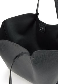 Bolso tote de cuero negro con superficie texturizada, parte superior abierta y dos asas resistentes. El interior es suave con un detalle de cierre a presión.