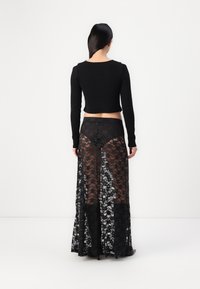 Zwarte geribbelde crop top gecombineerd met een doorschijnende zwarte kanten rok. De rok heeft bloemenpatronen en een lange, vloeiende uitstraling.