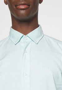 Camicia button-up azzurro chiaro con colletto a punta, con un piccolo logo "BOSS" ricamato in bianco sul lato sinistro. Tessuto dalla superficie liscia.