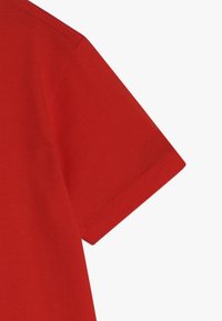 Manica di t-shirt in cotone rosso, design aderente con una texture liscia, caratterizzata da un orlo cucito e un bordo dritto.