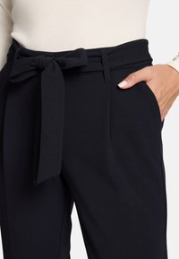 Pantalon bleu marine sur mesure avec une large ceinture et une ceinture en tissu nouée. Comprend des poches avant et une finition lisse et texturée.