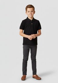 Czarna koszulka polo z krótkimi rękawami, z trzema guzikami i brązowym guzikiem. Połączona z szarymi spodniami i brązowymi butami.