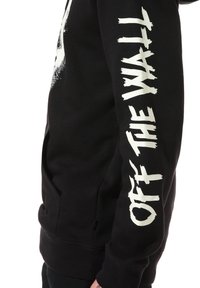 Sudadera negra con un acabado texturizado. Presenta un gran texto blanco "OFF THE WALL" en la manga y un bolsillo tipo canguro. Diseño con capucha.