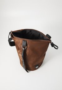 Sac seau en tissu marron avec texture florale, zip noir, bandoulière amovible et patch logo à la base. L'intérieur est uni noir.