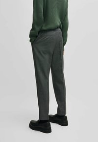 Gray textured trousers featuring a slim fit, side pockets, and a smooth waistband, paired with black platform shoes and a dark green sweater.