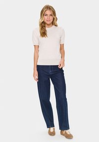 Světle béžový svetr s krátkým rukávem a žebrovaným lemem doplněný tmavě modrými širokými džíny. Oblečení doplňují hnědé boty.