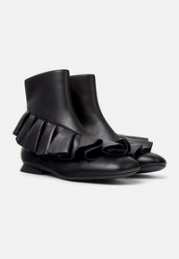 Zwarte leren enkellaarsjes met een ruchesaccent rondom de basis. Platte zool en afgeronde neus. Soepele textuur met een minimalistische stijl.