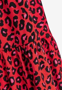 Tissu rouge avec un motif léopard irrégulier en noir et rose et des détails de couture froncée.