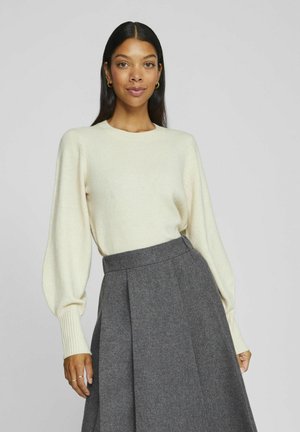 Light cream sweater with long, slightly puffed sleeves, paired with a high-waisted, dark gray wool skirt featuring pleats. Smooth texture.
