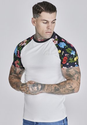 Tricou alb, ajustat, cu mâneci scurte decorate cu un model floral colorat, tiv negru și un mic logo alb pe piept. Mâneci scurte și textură fină.