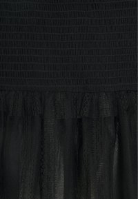 Czarna sukienka z teksturowaną, żebrowaną górną częścią oraz warstwowym, przezroczystym tiulem w falbanie u dołu. Gładki materiał o lekkiej konstrukcji.