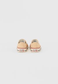 Beige vászon tornacipő lekerekített orral, alacsony profilú, látható varrásokkal, gumitalppal, és Converse All Star márkázással a sarkán.