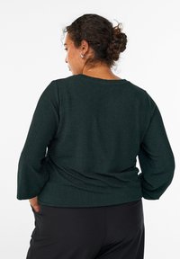 Zielony sweter o textured, z długimi rękawami, luźnym kroju i okrągłym dekoltem. Rękaw jest lekko zgromadzony z tyłu.