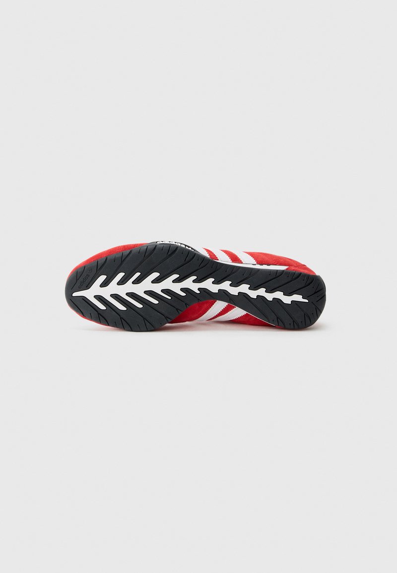 Basket rouge avec semelle noire et blanche, comportant trois bandes blanches et le logo Adidas sur la semelle extérieure, vue par le dessous.