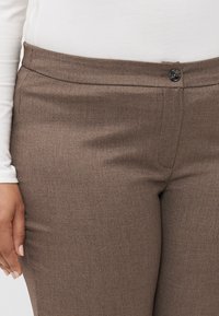 Pantalons marron ajustés avec une texture lisse, dotés d'une fermeture à bouton à l'avant, de passants de ceinture et de poches latérales.