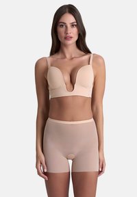 Reggiseno imbottito beige con scollatura profonda e spalline regolabili, abbinato a pantaloni corti a vita alta, trasparenti e con design senza cuciture.