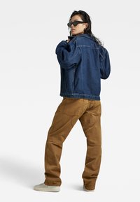 Donkerblauwe spijkerjas in oversized pasvorm met verlaagde schouders; gecombineerd met bruine cargobroek met zakken en naden. Lichtgewicht sneakers.
