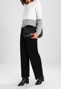 Dzianinowy sweter w kolorze białym i szarym, zestawiony z czarnymi spodniami o szerokich nogawkach oraz czarnymi botkami na obcasie. Modelka trzyma czarną teksturowaną torebkę.